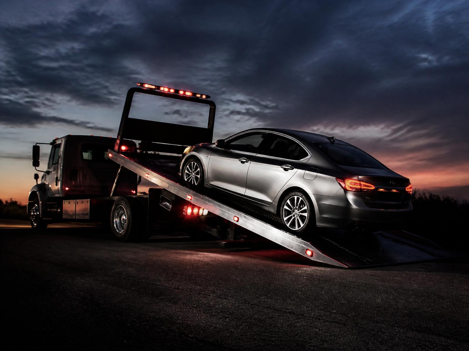Flatbed tow truck loading a disabled sedan at dusk